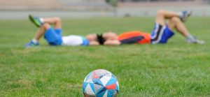 twee voetballers liggen op het veld een rekoefening bovenbeen te doen