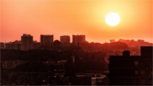 de skyline van een grote stad waar de zon aan het opkomen is en voor een oranje kleur in de lucht zorgt