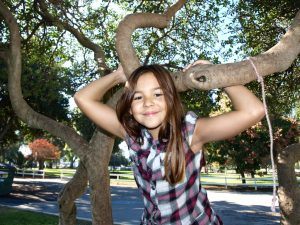 een meisje kijkt vrolijk en hangt aan een grote boomtak