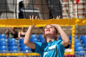 een meisje staat bij een volleybalnet en kijkt omhoog om een bal op te vangen