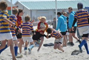 jongeren spelen ruby op het strand en een meisje met de bal wordt tegengehouden door een speler van het andere team