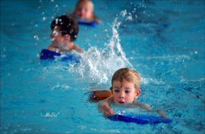 3 kindjes zwemmen met een drijfplankje in het zwembad
