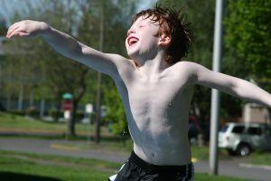 Een jongetje springt vrolijk in de lucht terwijl hij nat is van het zwemwater