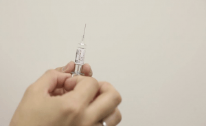 je ziet een vaccinatie spuit die wordt vastgehouden in een hand terwijl er tegenaan getikt wordt