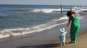 een moeder loopt met haar dochtertje langs het water op het strand