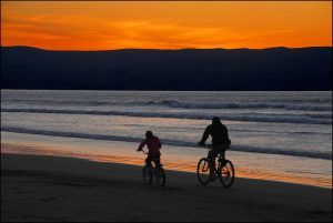 Een vader en zoon fietsen langs het strand tijdens zonsondergang