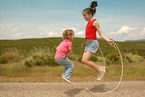 2 meisjes zijn samen aan het touwtjespringen en gebruiken daarvoor 1 touw