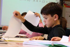 Een jongen zit in de klas en haalt een papiertje uit zijn map