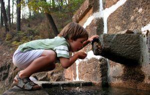 Een kindje vangt water met zijn hand op dat vanuit een bron uit de muur komt