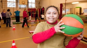 Vrouw staat in een gymzaal en houdt een gekleurde bal omhoog