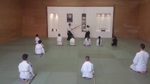 2 volwassen geven een demonstratie aikido tijdens een les en kinderen zitten te kijken