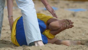 iemand ligt geblesseerd in het zand en grijpt naar zijn voet