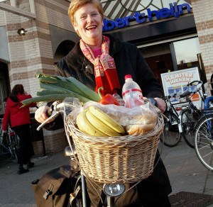 Een vrouw staat met haar fiets voor de Albert Heijn met een mand die gevuld is met groente en fruit