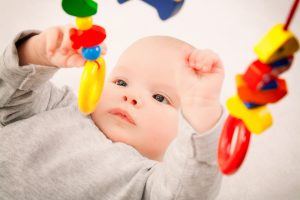 Een baby ligt op zijn rug en probeert een gekleurde ring die erboven hangt te grijpen