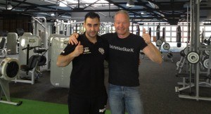 2 mannen in een fitnessruimte staan naast elkaar en steken een duim omhoog