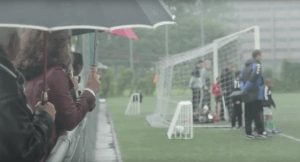 Ouders die in de regen aan de zijlijn staan bij een voetbalwedstrijd