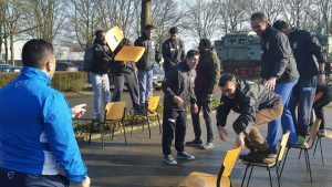 een groep vluchtelingen die tijdens een training een stoelendans doen