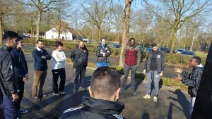 vluchtelingen die in de cursus Citytrainer luisteren naar de uitleg van een sportactiviteit