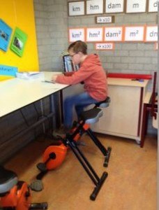 Een jongen zit in de klas op een fiets stoel aan een tafel te lezen