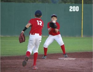 1 jonge honkballer gooit de bal naar een andere speler die bij een honk staat