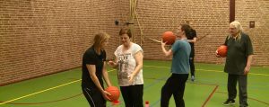 Buurtbewoners in een gymzaal aan het sporten met basketballen