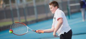 Jongen op de tennisbaan slaat een tennisbal met zijn racket