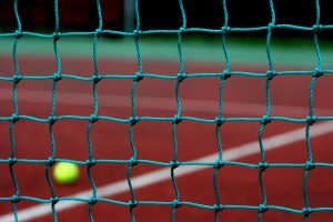 een close up van een tennisnet met een tennisbal op de achtergrond