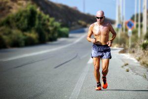 een afgetrainde man loopt hard zonder shirt in de zon langs de weg