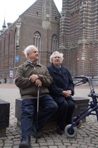 een oudere man en vrouw zitten samen op een bankje in het centrum van een stad