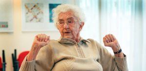 een oudere vrouw doet een beweegoefening uit Fit & Sterk waaier