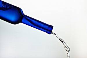 een blauwe fles die gekanteld wordt en waar een waterstraal uit komt