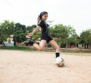 een jonge vrouw gaat een trap tegen een voetbal geven op een zanderige ondergrond