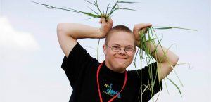 Een jongen met beperking neemt een grappige houding aan, met graspollen in zijn handen die hij tegen zijn hoofd houdt