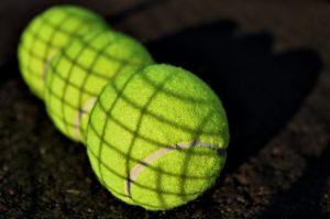 3 tennisballen liggen naast elkaar en je ziet de schaduw van het net op de ballen