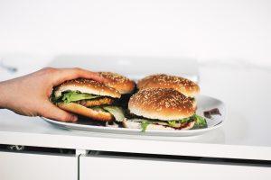 een hand grijpt naar een broodje hamburger die op een bord ligt met nog 2 broodjes hamburger