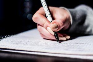 een vrouwenhand die met een pen iets opschrijft in een schriftje