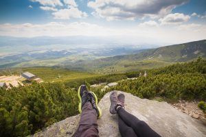 2 paar voeten van mensen die op de rand van een klif liggen en uitkijken over een mooie bosrijke vallei