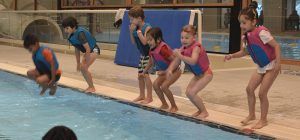 kinderen tijdens een zwemles staan op de rand van een zwembad en springen er in