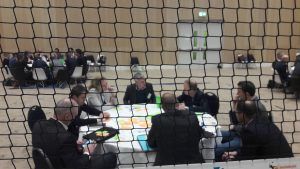 je kijkt door een net heen en ziet deelnemers aan de werkconferentie aan tafels in het zand zitten