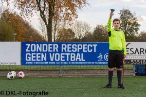 een jeugdscheidsrechter houdt een groene driehoek omhoog en staat op het veld naast een bord met de tekst zonder respect geen voetbal