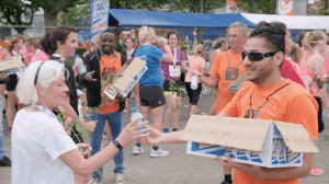Vrijwilliger in oranje shirt deelt water uit aan wandelaars