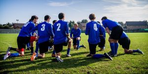 een sportploeg zit bij elkaar op het gras, om iets met elkaar te bespreken