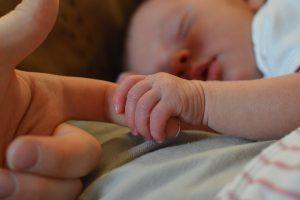een baby slaapt en houdt met zijn handje de vinger van moeder vast