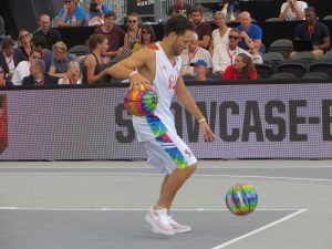 een man dribbelt met 2 gekleurde ballen terwijl publiek op de tribune toekijkt