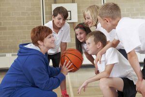 Kinderen krijgen uitleg van een vrouw over basketbal