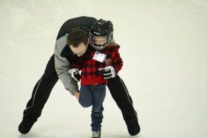 Een ouder ondersteunt jong kind bij het schaatsen