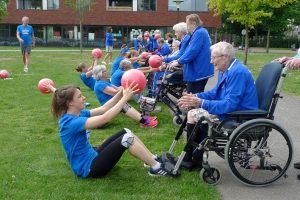 sporters doen een bal oefening met ouderen die in een rolstoel zitten of achter een rollator staan