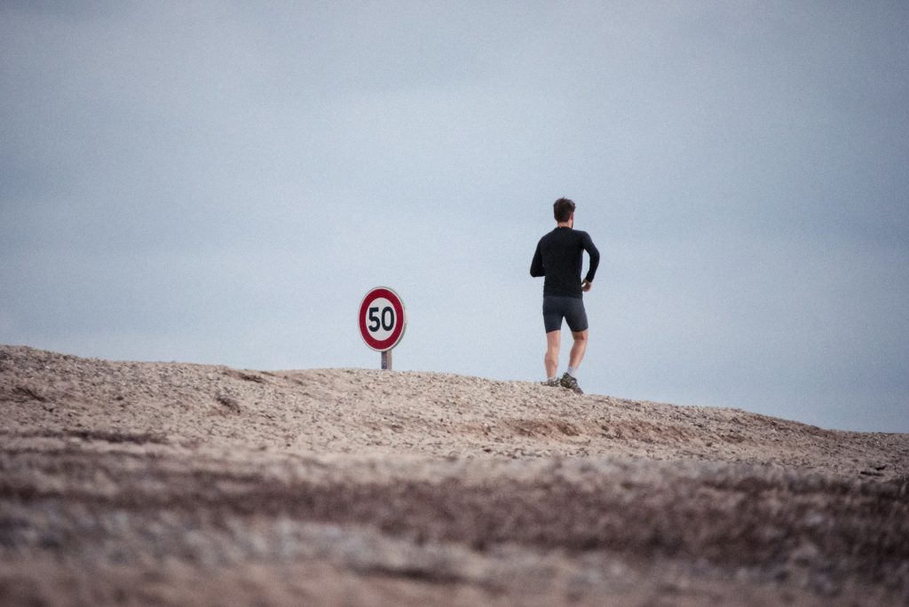 een jogger op kale rotsachtige bodem met als enige object in de buurt een verkeersbord max. 50 km 