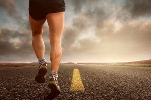 de gespierde benen van een man die aan het hardlopen is op een lange geasfalteerde weg