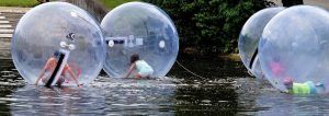kinderen die apart van elkaar in een grote plastic bal zitten en bewegen op het water